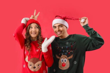 Kırmızı arka planda Noel süveteri giyen, sevgi dolu çift.