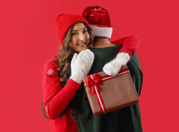 Young Woman Christmas Gift Hugging Her Beloved Boyfriend Red Background — Stock Photo, Image