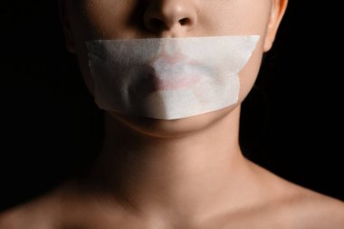 Karanlık arka planda ağzı bantlı genç bir kadın, yakın plan. Sansür kavramı