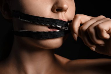 Ağzında fermuarı koyu arka planda olan genç bir kadın, yakın plan. Sansür kavramı
