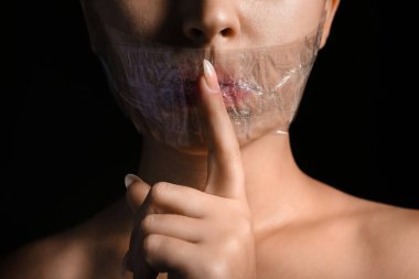Ağzı bantlı genç bir kadın karanlık arka planda sessizlik jesti yapıyor, yakın plan. Sansür kavramı