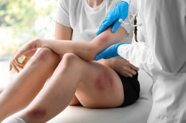 Kadın doktor klinikte hastanın yaralı kolunu muayene ediyor.