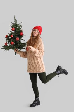 Gri arka planda Noel ağacı ve dekoru olan genç bir kadın.