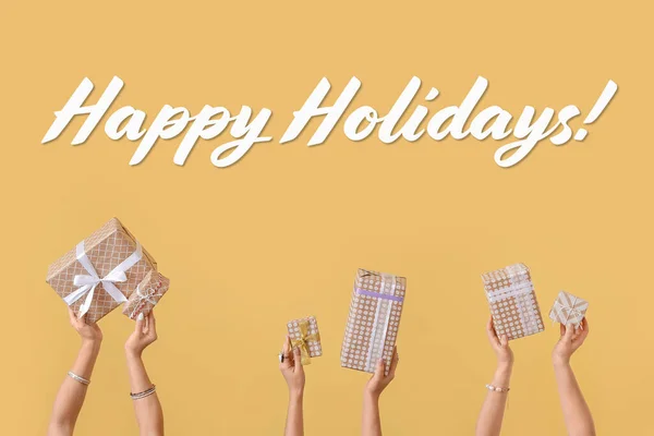 Hands with gift boxes on yellow background. Happy holidays