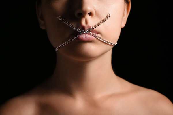 Молодая женщина с цепью во рту на тёмном фоне. Концепция цензуры