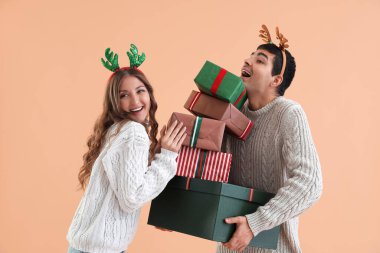 Bej arka planda Noel hediyeleriyle ren geyiği boynuzları takan sevimli çift