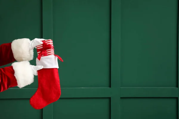 Santa Claus with Christmas sock and present near green wall