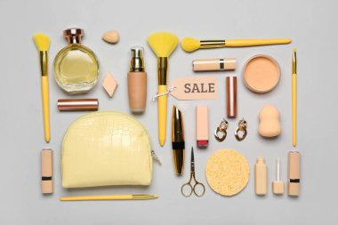 Kozmetik ürünleri, aksesuarlar ve gri arka planda satış etiketi olan sarı çanta.