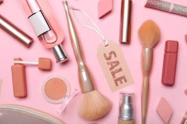 Kozmetik ürünleri, aksesuarlar ve pembe arka planda satış etiketi olan çanta.