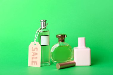 Yeşil arka planda ruj ve satış etiketli parfüm şişeleri