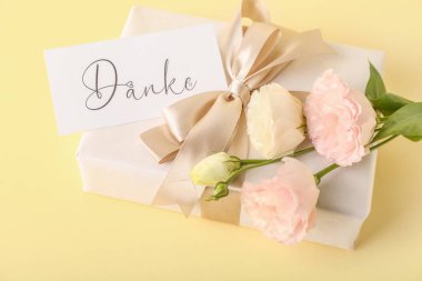 Hediye kutusu, içinde DANKE yazan kart ve renk arkaplan üzerinde Eustoma çiçekleri, yakın plan