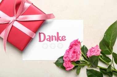 DANKE yazılı kart, hediye kutusu ve arka planda gül çiçekleri