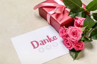 DANKE yazılı kart, hediye kutusu ve arka planda gül çiçekleri, yakın plan