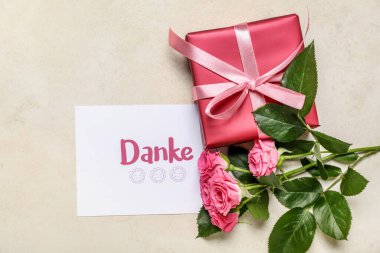 DANKE yazılı kart, hediye kutusu ve arka planda gül çiçekleri