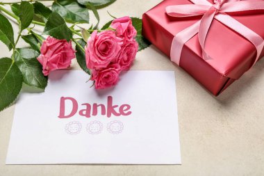 DANKE yazılı kart, hediye kutusu ve arka planda gül çiçekleri, yakın plan