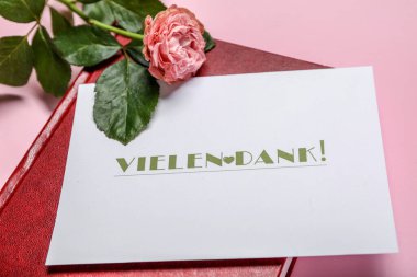 Üzerinde VİELEN DANK yazan kart, pembe arkaplanda defter ve gül çiçeği, yakın plan