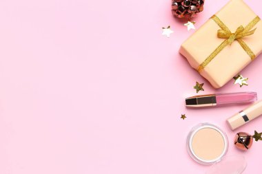 Noel çanlı makyaj ürünleri ve pembe arka planda hediye.