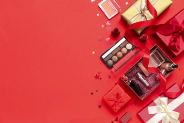 Makyaj ürünleri ve kırmızı arka planda Noel dekoru olan hediye kutuları.