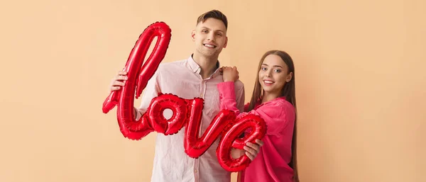 一对年轻夫妇的气球形状的字爱的米色背景 情人节庆祝活动 — 图库照片