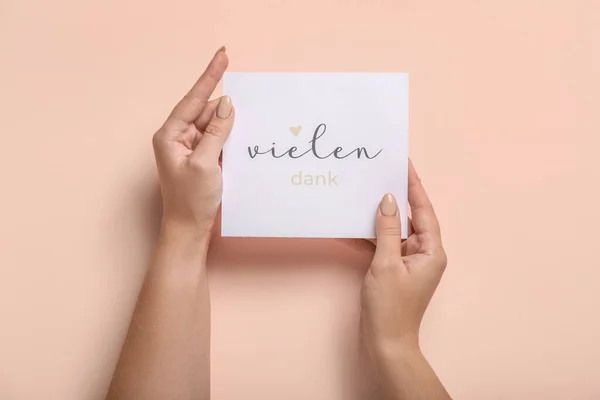 Woman holding card with text VIELEN DANK on color background, closeup