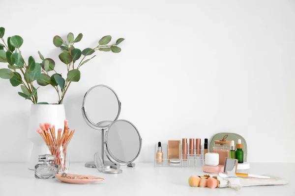 stock image Different cosmetics, makeup accessories and mirrors on table against light wall