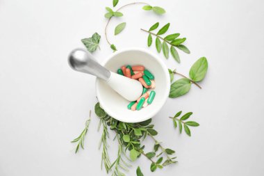 Mortar with pills and different herbs on white background clipart