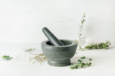 Taş havan, şifalı otlar ve haplar beyaz ahşap masada.