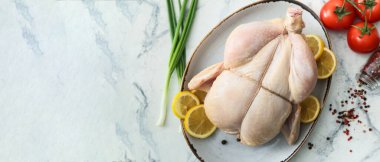 Tabakta çiğ tavuk, limon, sebze ve baharatlar var. Arka planda hafif arkaplan ve metin için yer var.