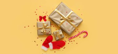 Sarı arka planda Noel hediyeleri, eldivenler ve şeker kamışlarıyla kompozisyon