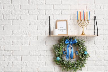 Shelf with menorah for Hanukkah, frame and wreath hanging on white brick wall clipart