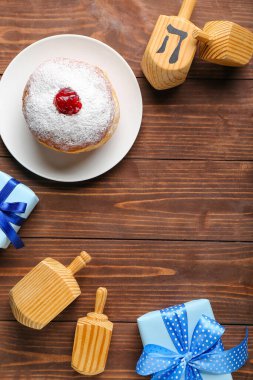 Ahşap arka planda Hanuka kutlaması için lezzetli donut, dreidels ve hediyelerle yapılmış çerçeveler.