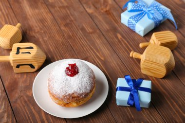 Ahşap arka planda Hannukah kutlaması için lezzetli donut, dreidels ve hediyelerle dolu bir tabak.