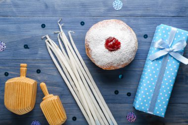 Dreidels, mumlar ve mavi ahşap arka planda Hannukah kutlaması için hediyeli lezzetli donut.