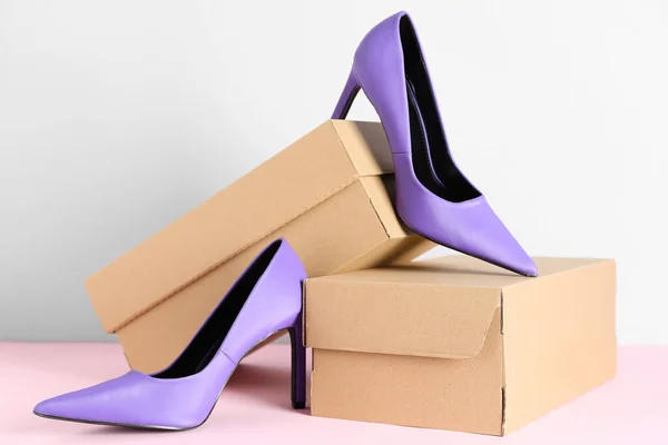 白い壁の近くのテーブルの上に紫色のハイヒールの靴を持つ段ボール箱 — ストック写真