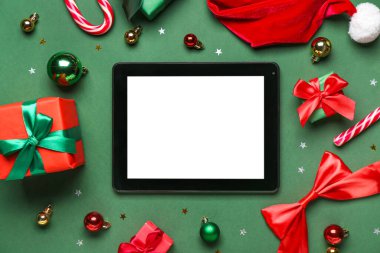 Yeşil arka planda şeker kamışlı, hediyeli ve Noel dekorlu bir tablet bilgisayar.