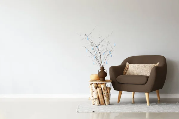 Grey sofa with Easter decor and basket with firewood near light wall in room
