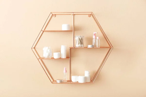 Shelves with container of soft cotton wool, swabs and cosmetic bottles on beige wall