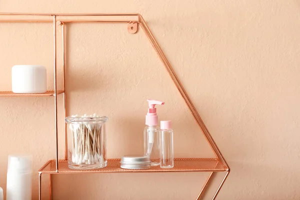 Shelves with container of swabs and cosmetic bottles on beige wall