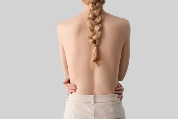 Blonde woman with naked back and pigtail hairstyle on light background