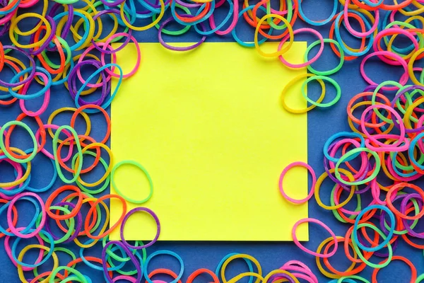 Sticky note and colorful rubber bands on blue background