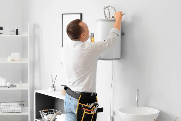 Male plumber repairing electric boiler with wrench in bathroom