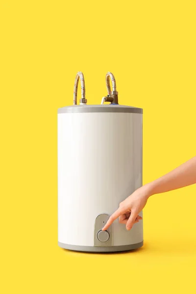 Woman adjusting electric boiler on yellow background