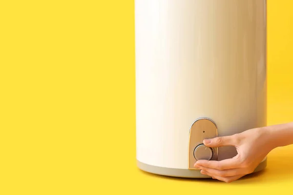 Woman adjusting electric boiler on yellow background, closeup