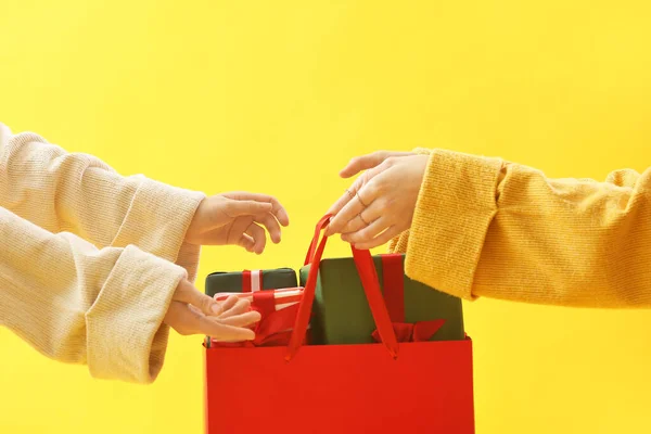 Women with bag of Christmas gifts on yellow background