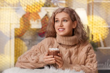 Güzel genç bayan Noel arifesinde evde sıcak kakao içiyor.