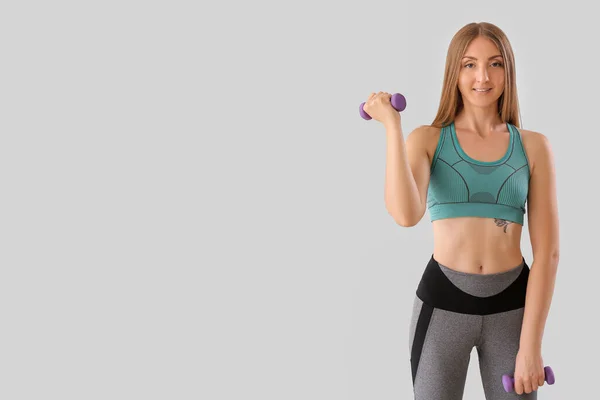 stock image Sporty young woman with dumbbells on light background