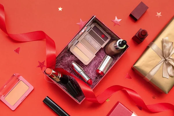 Gift boxes with makeup products and Christmas decor on red background