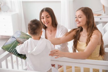 Mutlu lezbiyen çift ve yatak odasında kitabı olan küçük bebekleri