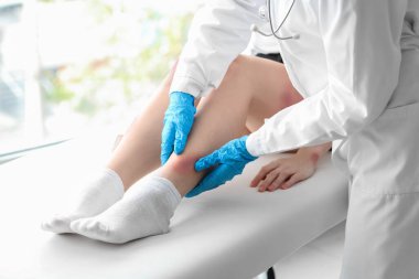 Kadın doktor klinikte yaralı bacağını muayene ediyor.