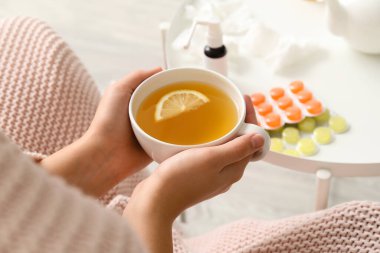 Evde boğazı ağrıdığı için limon çayı içen kadın, yakın plan.